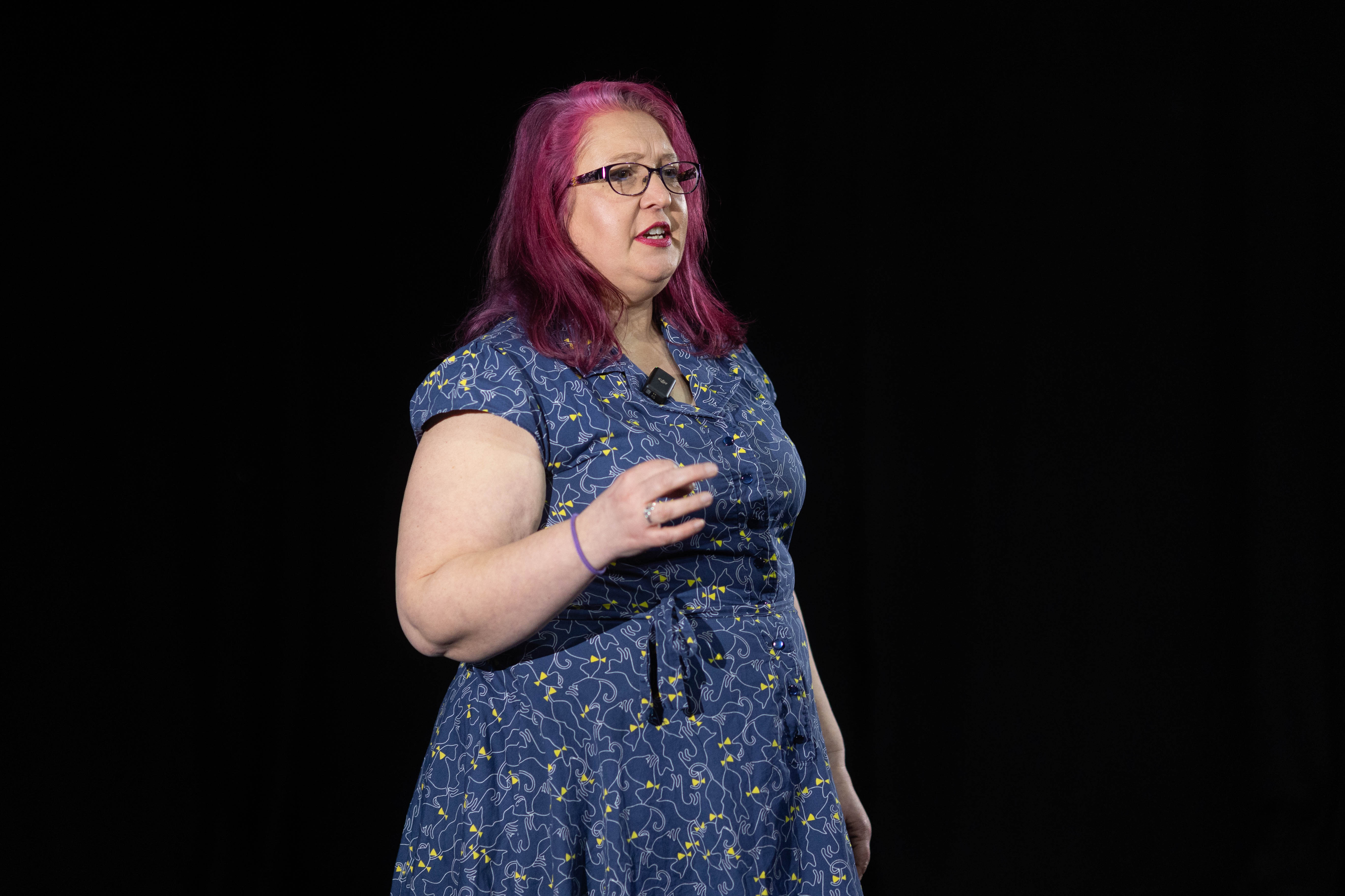 Woman in a blue dress with red hair walking confidently onto a stage with the audience int he forground in silhouette
